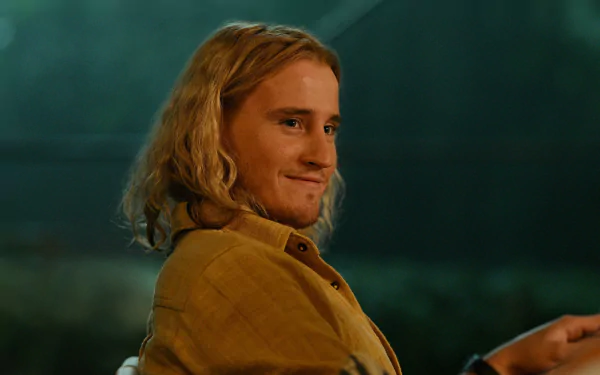 A character from the TV show Apples Never Fall smiles warmly, set against a softly lit background. This HD desktop wallpaper captures a moment of charm and intrigue.