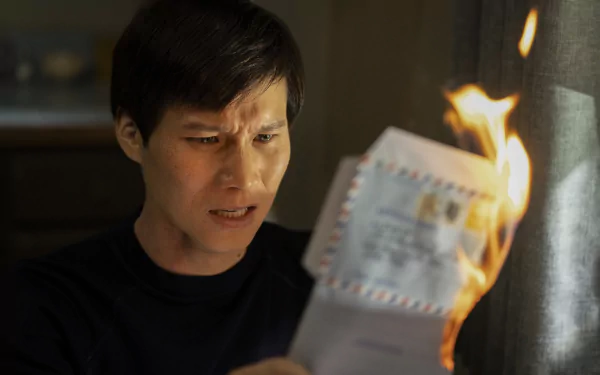 HD wallpaper from The Sympathizer TV show featuring a character intently looking at a burning piece of paper.