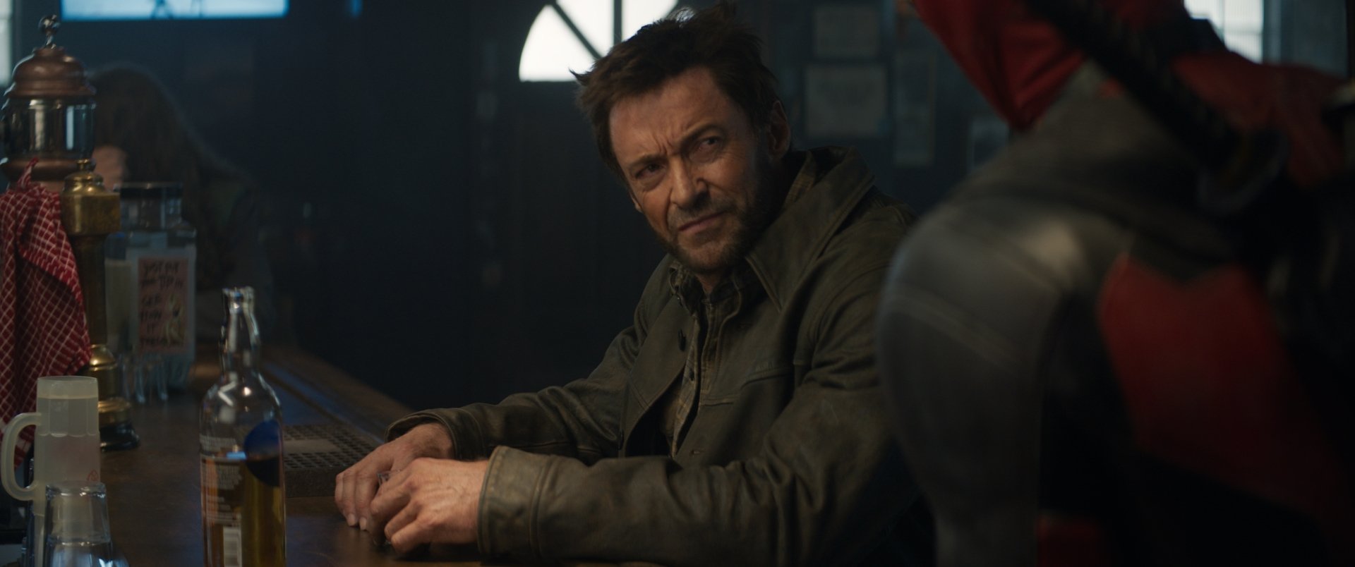 HD desktop wallpaper from a movie scene featuring Wolverine sitting at a bar with Deadpool partially visible in the background.