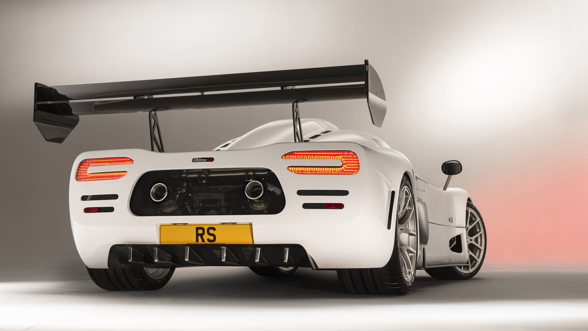HD desktop wallpaper featuring the rear view of a white Ultima RS sports car with distinctive aerodynamic wing and RS license plate.