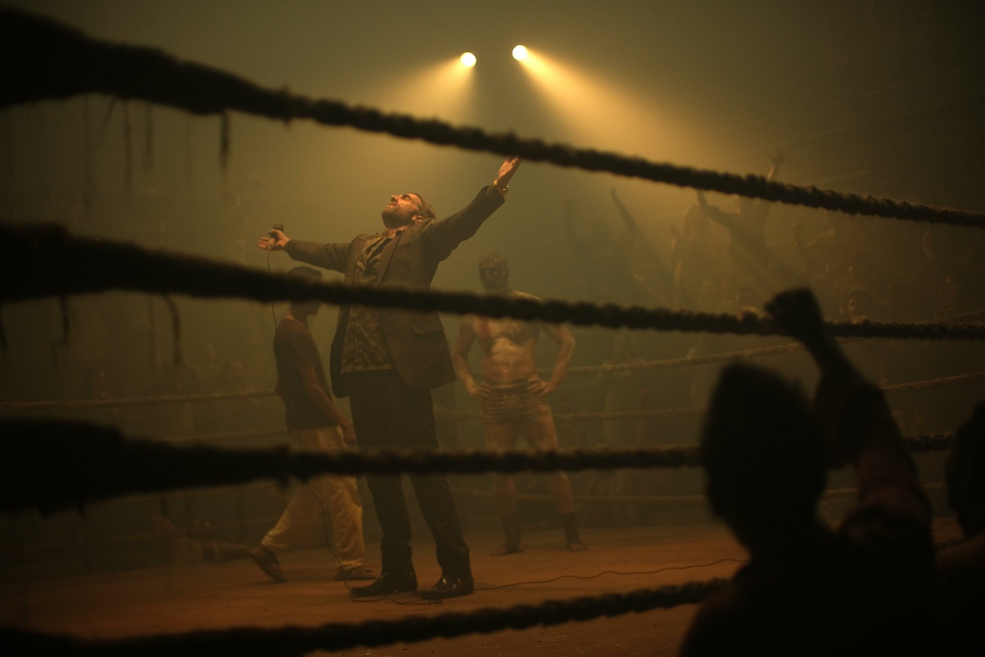 HD wallpaper featuring a dramatic scene from the movie Monkey Man (2024) with a man triumphantly raising his arms in a smokey, dimly-lit boxing ring.