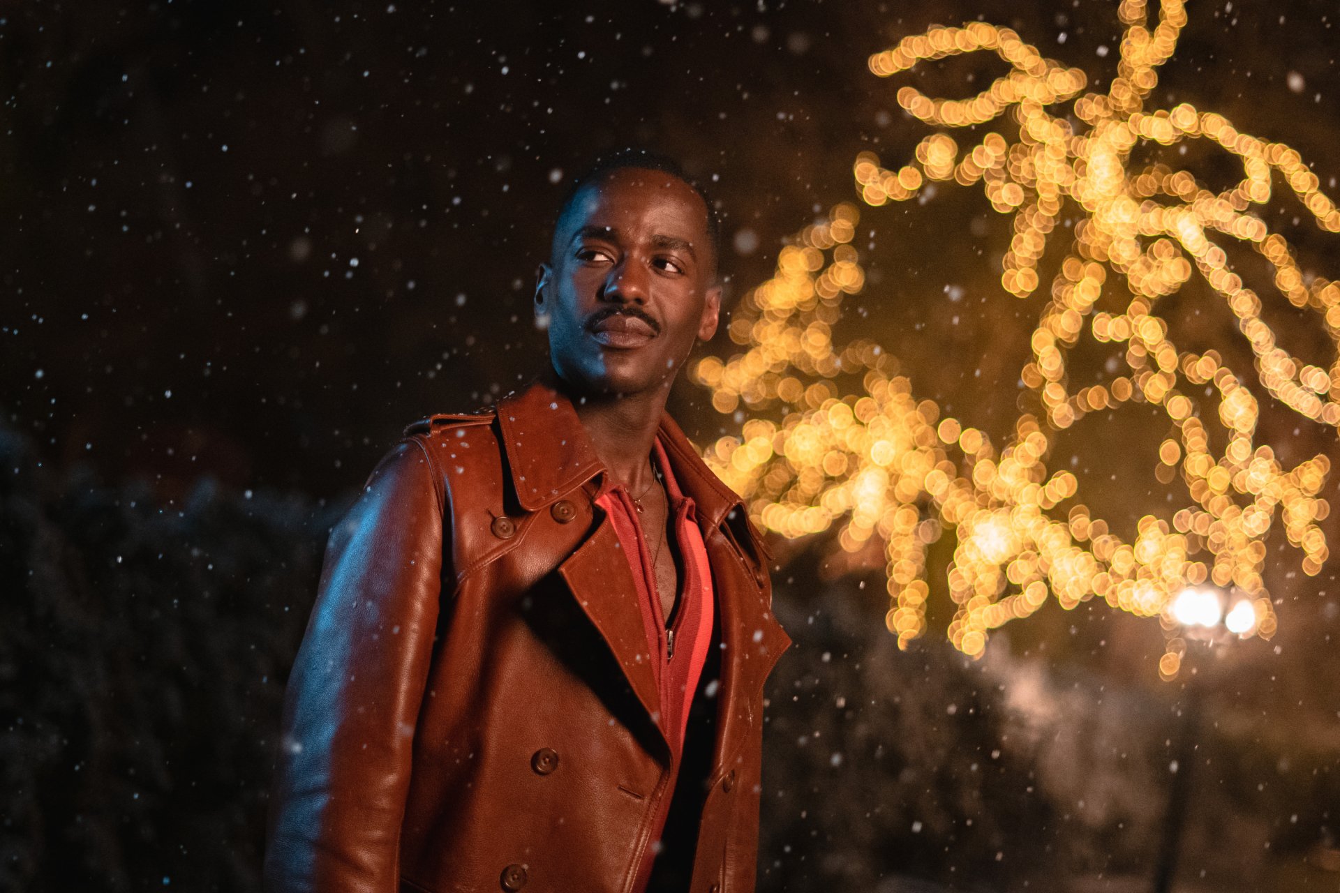 HD desktop wallpaper of Ncuti Gatwa from Doctor Who (2023), standing in a snowy scene with glowing lights in the background.