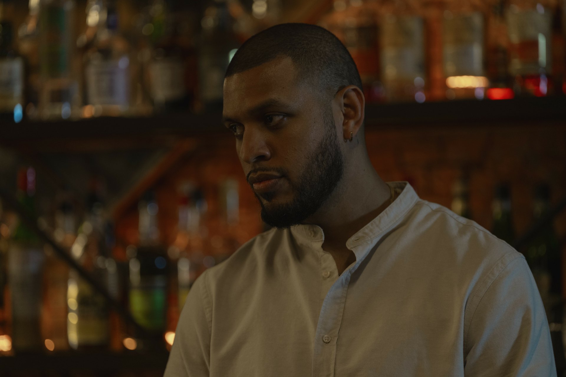 A HD desktop wallpaper featuring a scene from the TV Show Presumed Innocent (2024) with a man standing in a dimly-lit bar.