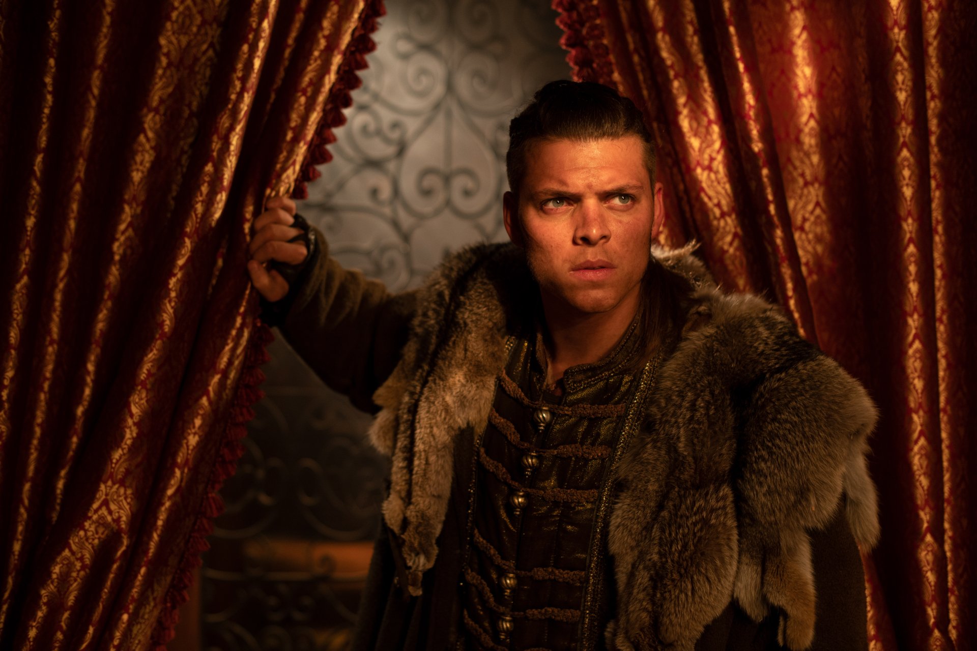 HD desktop wallpaper featuring Ivar The Boneless from the TV show Vikings (2013). Ivar stands between luxurious red curtains, dressed in fur, with an intense expression on his face.