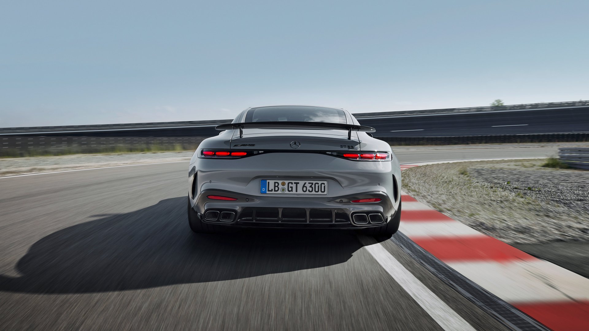 HD desktop wallpaper featuring the rear view of a sleek Mercedes-AMG GT63 PRO driving on a racetrack, highlighting its powerful design and speed against a clear sky.