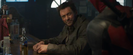 HD desktop wallpaper from a movie scene featuring Wolverine sitting at a bar with Deadpool partially visible in the background.