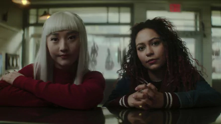 Two young women from the TV show Dead Boy Detectives sit side by side, staring directly at the camera. This HD desktop wallpaper and background image captures a contemplative scene with muted tones.