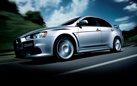 HD desktop wallpaper featuring a sleek silver Mitsubishi Lancer Evolution X speeding on a road with a backdrop of trees and a vibrant sky.