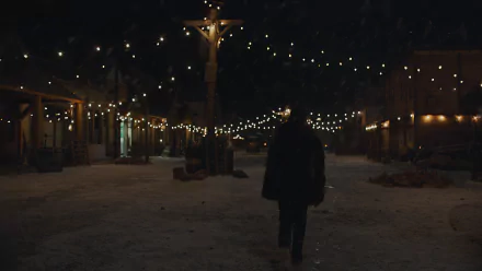 The Last Of Us 8K Ultra HD PC desktop wallpaper/background: lone figure walks down a snowy, string-lit town street at night, warm lamps and hanging lights casting a soft glow.