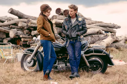 Desktop wallpaper from the movie The Bikeriders featuring Austin Butler and Jodie Comer, set against a backdrop of logs and a motorcycle.
