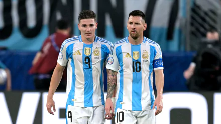 A high-definition desktop wallpaper featuring Lionel Messi and Julián Álvarez in their Argentina National Football Team jerseys during a soccer match.
