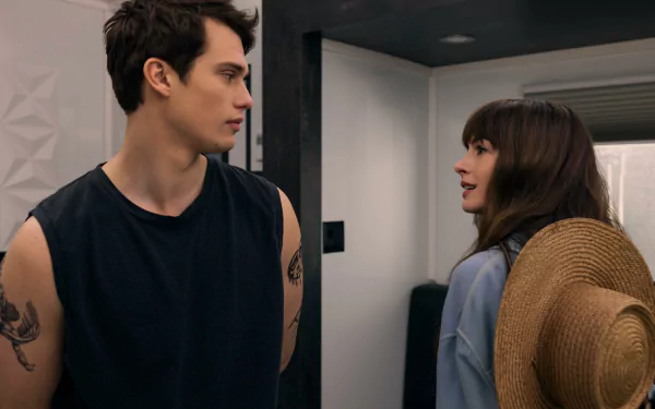 HD wallpaper featuring a scene from the movie The Idea of You with a young man and woman conversing in a modern interior setting.