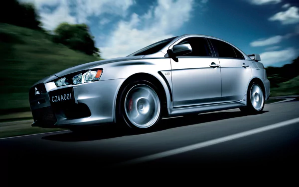 HD desktop wallpaper featuring a sleek silver Mitsubishi Lancer Evolution X speeding on a road with a backdrop of trees and a vibrant sky.