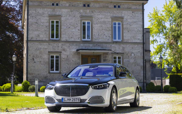 HD desktop wallpaper featuring a Mercedes-Maybach S 680 parked in front of an elegant stone building surrounded by greenery.