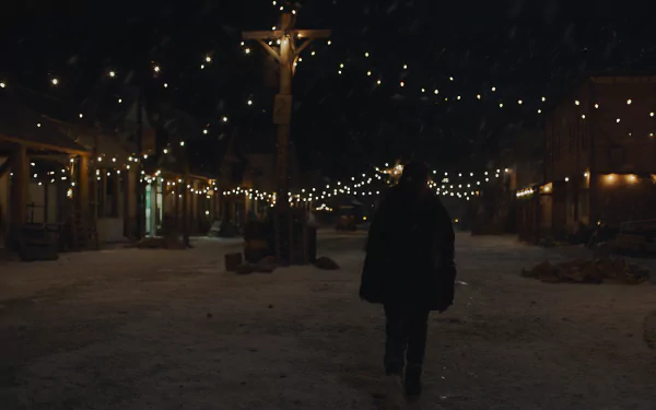 The Last Of Us 8K Ultra HD PC desktop wallpaper/background: lone figure walks down a snowy, string-lit town street at night, warm lamps and hanging lights casting a soft glow.