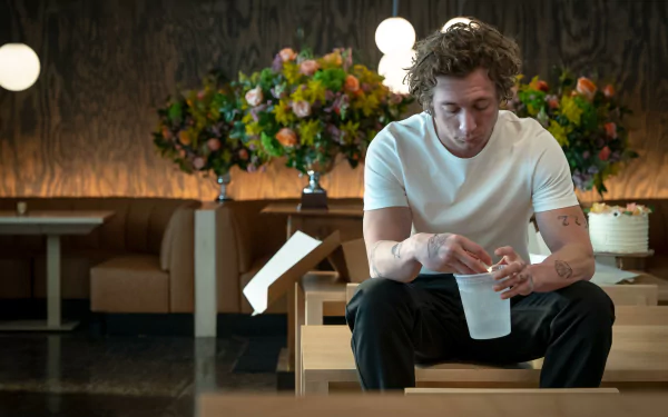 HD desktop wallpaper featuring Jeremy Allen White from the TV show The Bear, sitting in a restaurant with vibrant flowers in the background.