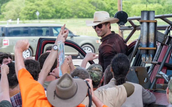 A scene from the movie Twisters showing a man in a cowboy hat smiling amidst a group of enthusiastic people, set as a HD desktop wallpaper and background.