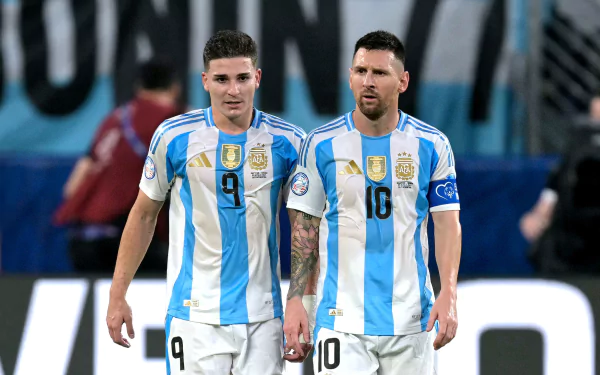 A high-definition desktop wallpaper featuring Lionel Messi and Julián Álvarez in their Argentina National Football Team jerseys during a soccer match.