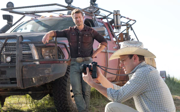 Scene from the movie Twisters featuring two men by a rugged vehicle, one standing and the other with a camera, in an outdoor setting. HD desktop wallpaper and background.