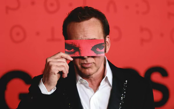 HD desktop wallpaper featuring a man holding a red card with eyes printed on it against a red background, tagged with movie and Longlegs.