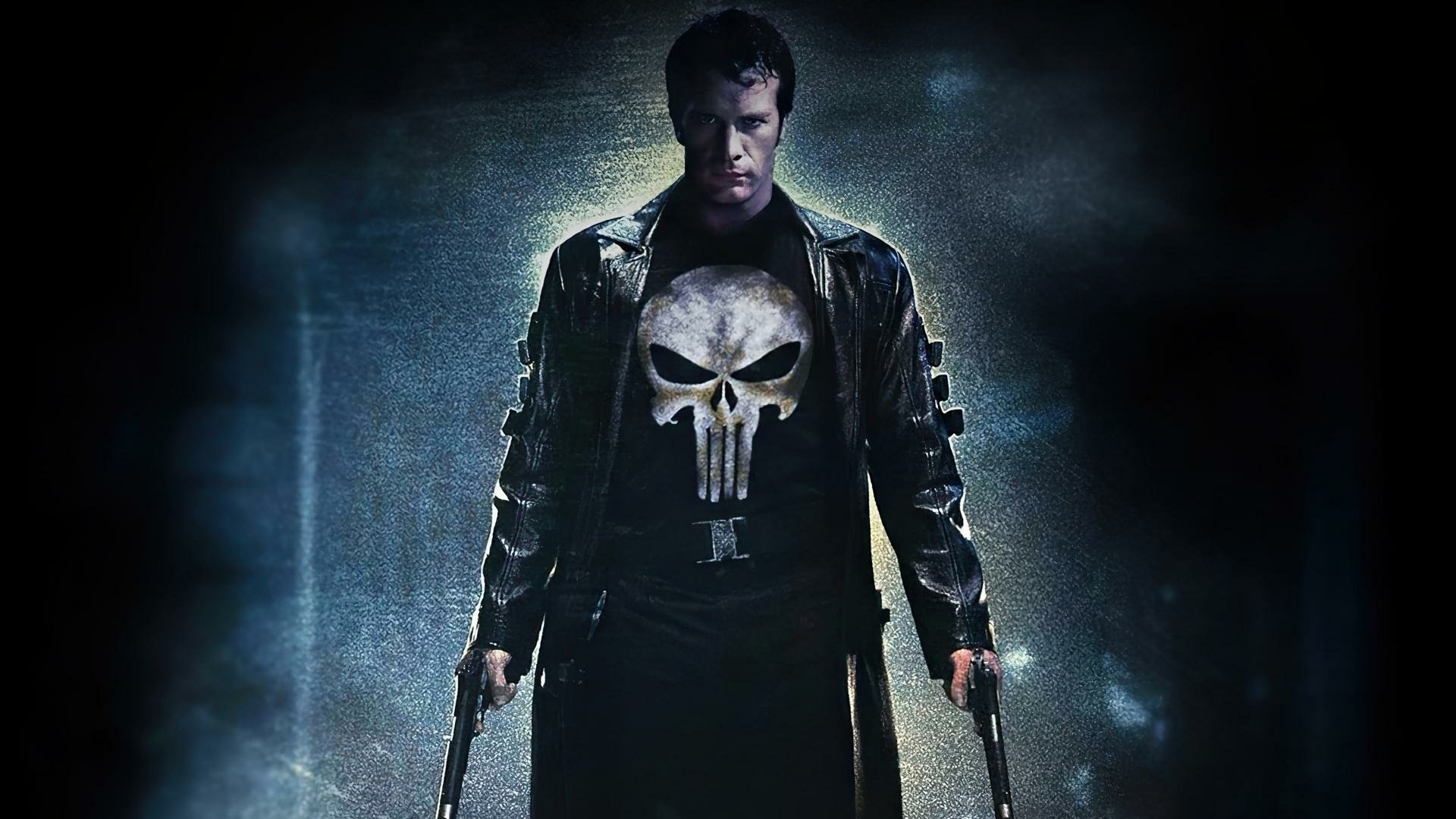 HD PC wallpaper: The Punisher (Marvel Comics) — trench-coated vigilante with skull shirt, dual pistols and moody cinematic lighting, shown in a live-action actor portrayal.