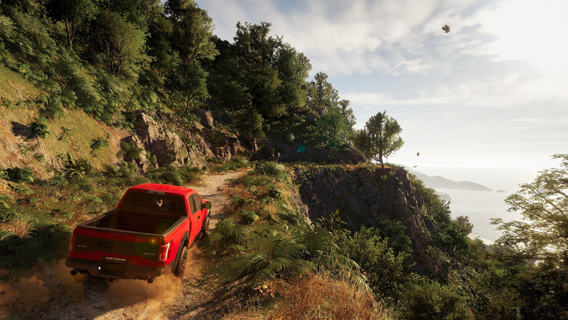 A vibrant scene from Test Drive Unlimited Solar Crown, featuring a red truck navigating a scenic, rugged path surrounded by lush greenery and a distant view of the ocean.