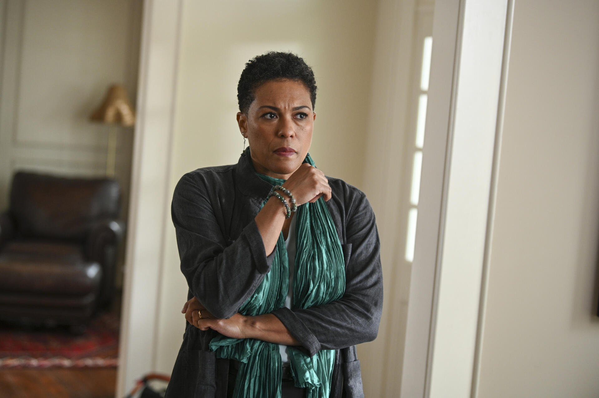 A dramatic scene from the TV show Tracker (2024), featuring a woman with a concerned expression, wearing a green scarf, set in a stylish indoor environment. HD wallpaper background.