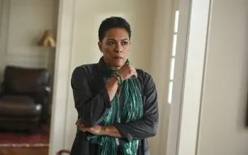 A dramatic scene from the TV show Tracker (2024), featuring a woman with a concerned expression, wearing a green scarf, set in a stylish indoor environment. HD wallpaper background.