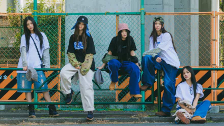 A stylish HD wallpaper featuring the K-pop group NewJeans, showcasing their unique fashion sense as they pose casually against an urban backdrop.