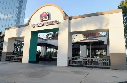 A high-definition desktop wallpaper showcasing a Taco Bell restaurant exterior, featuring modern architecture and outdoor seating under umbrellas.
