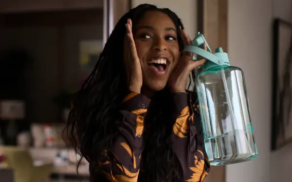 Jessica Williams joyfully poses with a water jug from the TV show Shrinking, in this vibrant 4K Ultra HD desktop wallpaper.