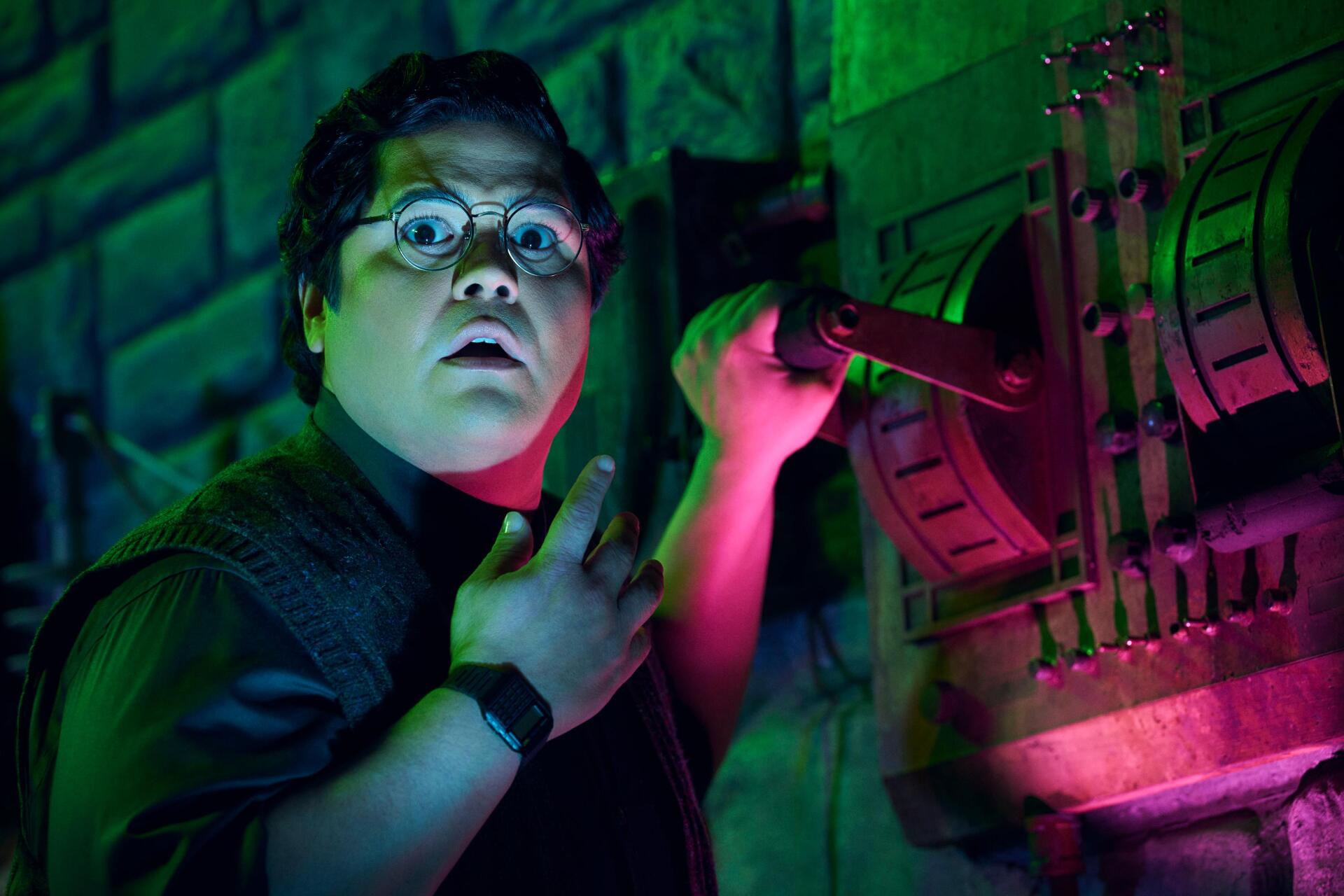 Harvey Guillén as Guillermo in a vibrant scene from What We Do in the Shadows, showcasing his expressive reaction against a colorful, moody backdrop. HD wallpaper for fans.