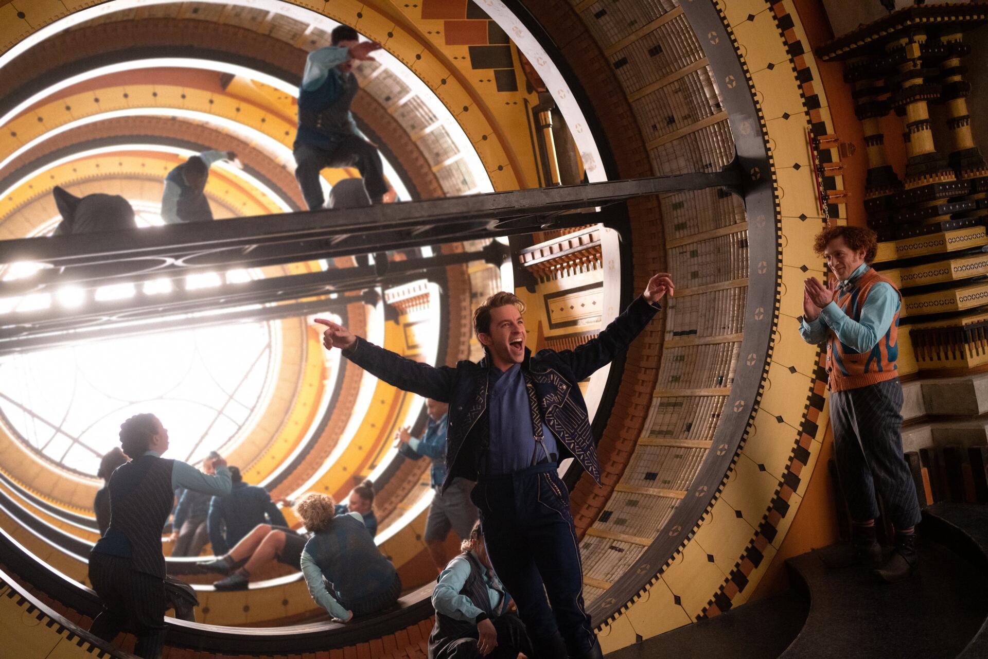 A dynamic scene from the movie Wicked, featuring Jonathan Bailey amidst a vibrant spiral backdrop, showcasing energetic movements and interactions in a theatrical setting.