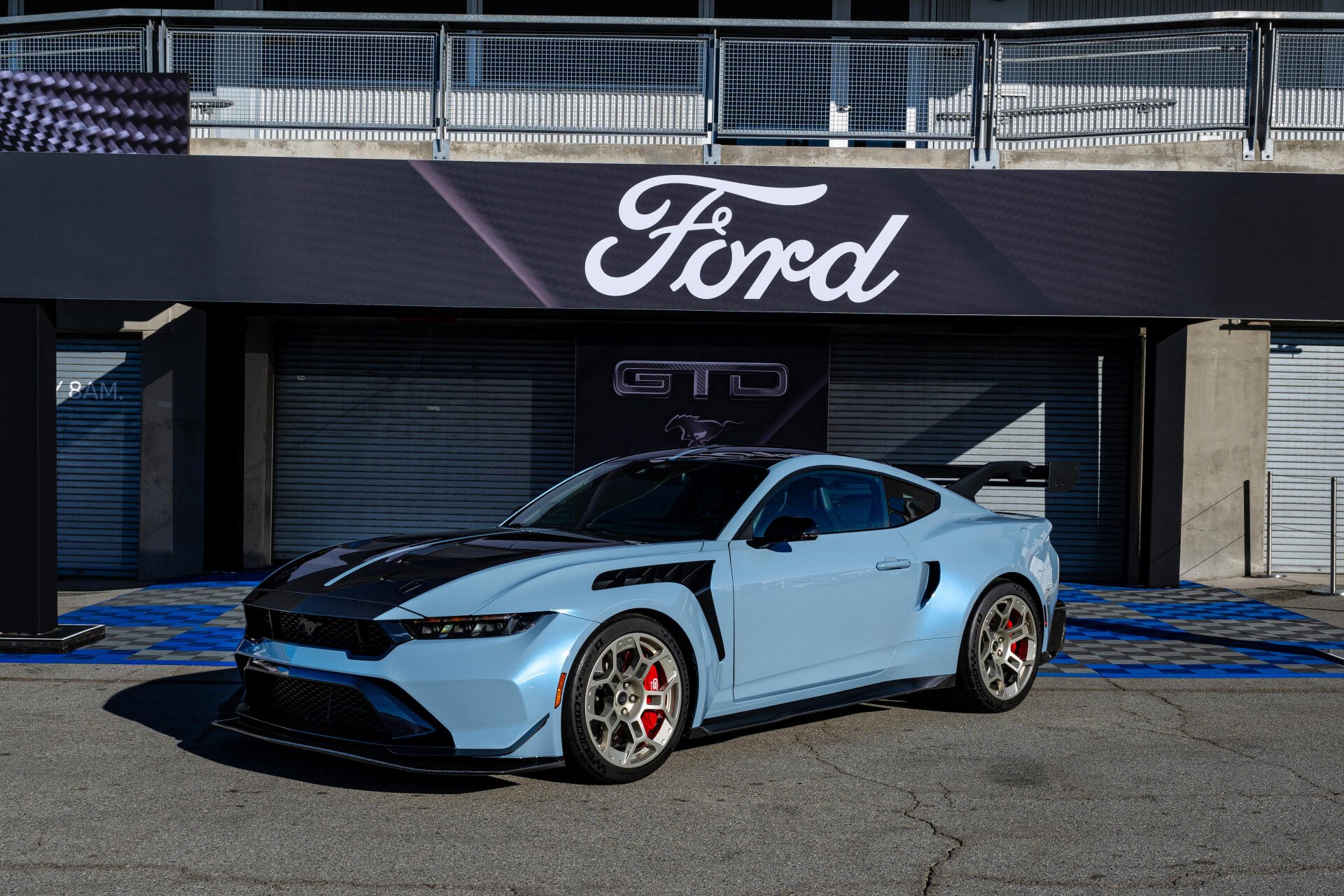 A sleek blue Ford Mustang GTD parked in front of a Ford sign, showcasing its modern design in a vibrant 4K Ultra HD backdrop. Ideal as a desktop wallpaper.