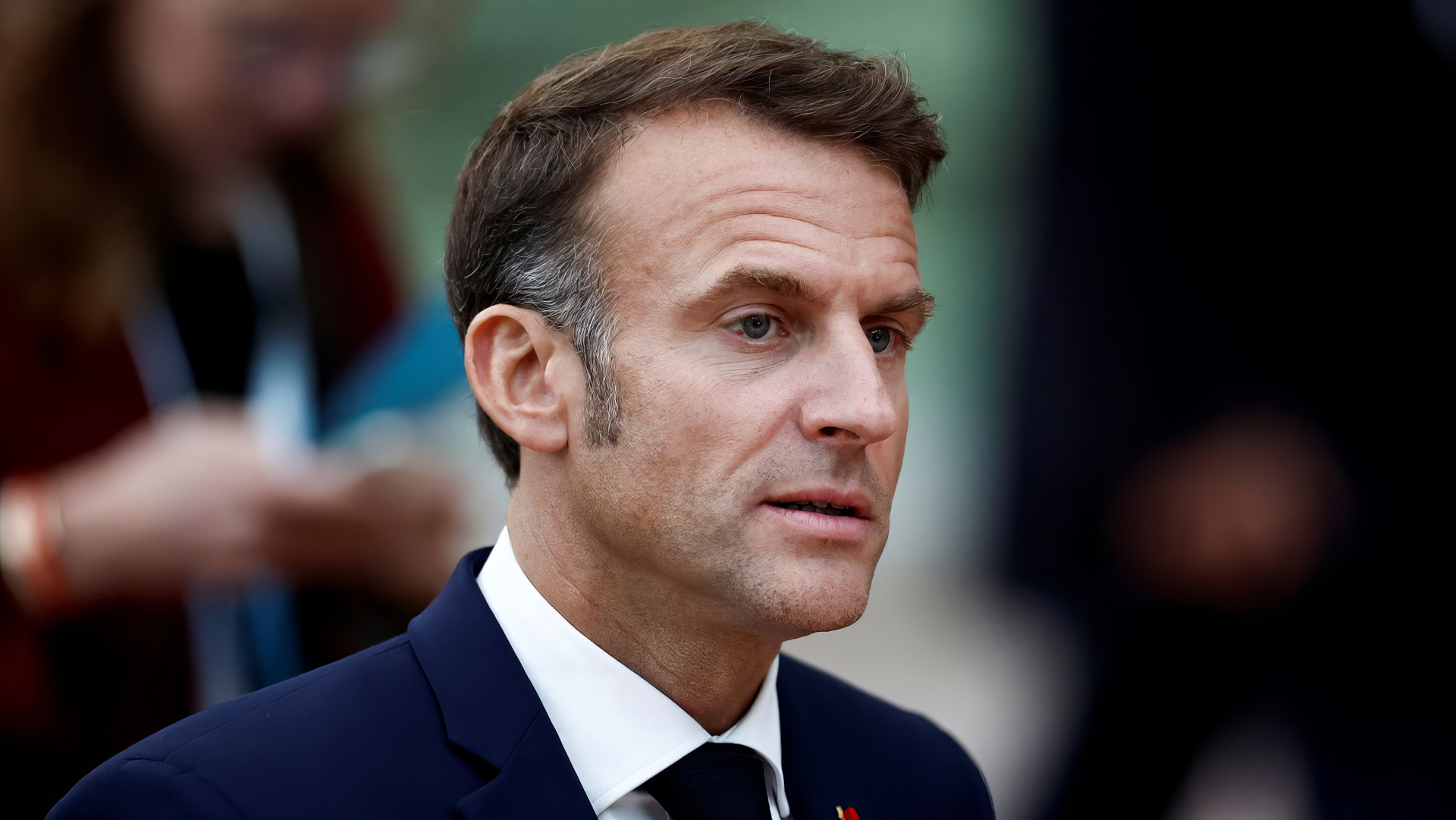 Close-up of Emmanuel Macron, dressed in a suit, with a thoughtful expression, set against a blurred background. This HD image serves as a striking desktop wallpaper and background.