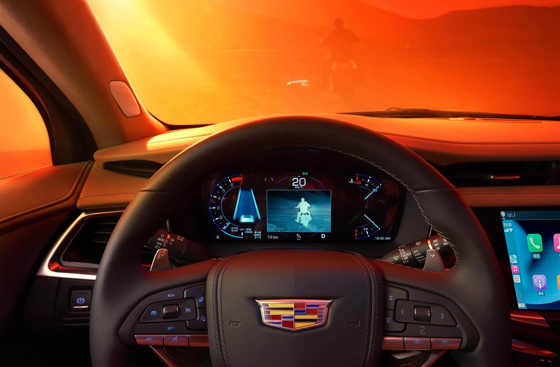 The image showcases the interior of a Cadillac XT6, featuring a vibrant orange backdrop and a view of the dashboard with advanced controls and display screens.