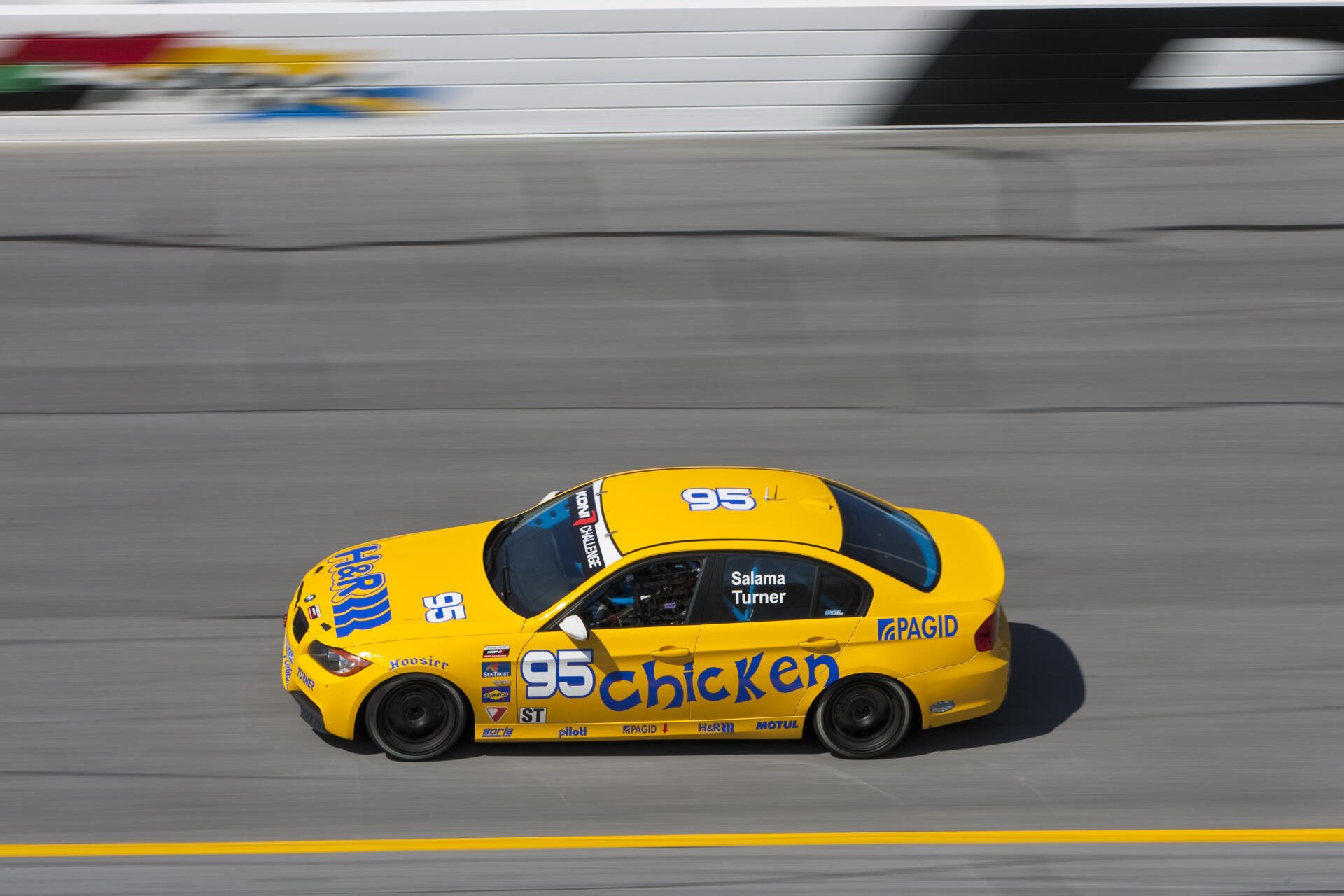 A vibrant yellow BMW E90 race car with 95 and Chicken branding speeds around a track, showcased as a high-definition PC desktop wallpaper and background.