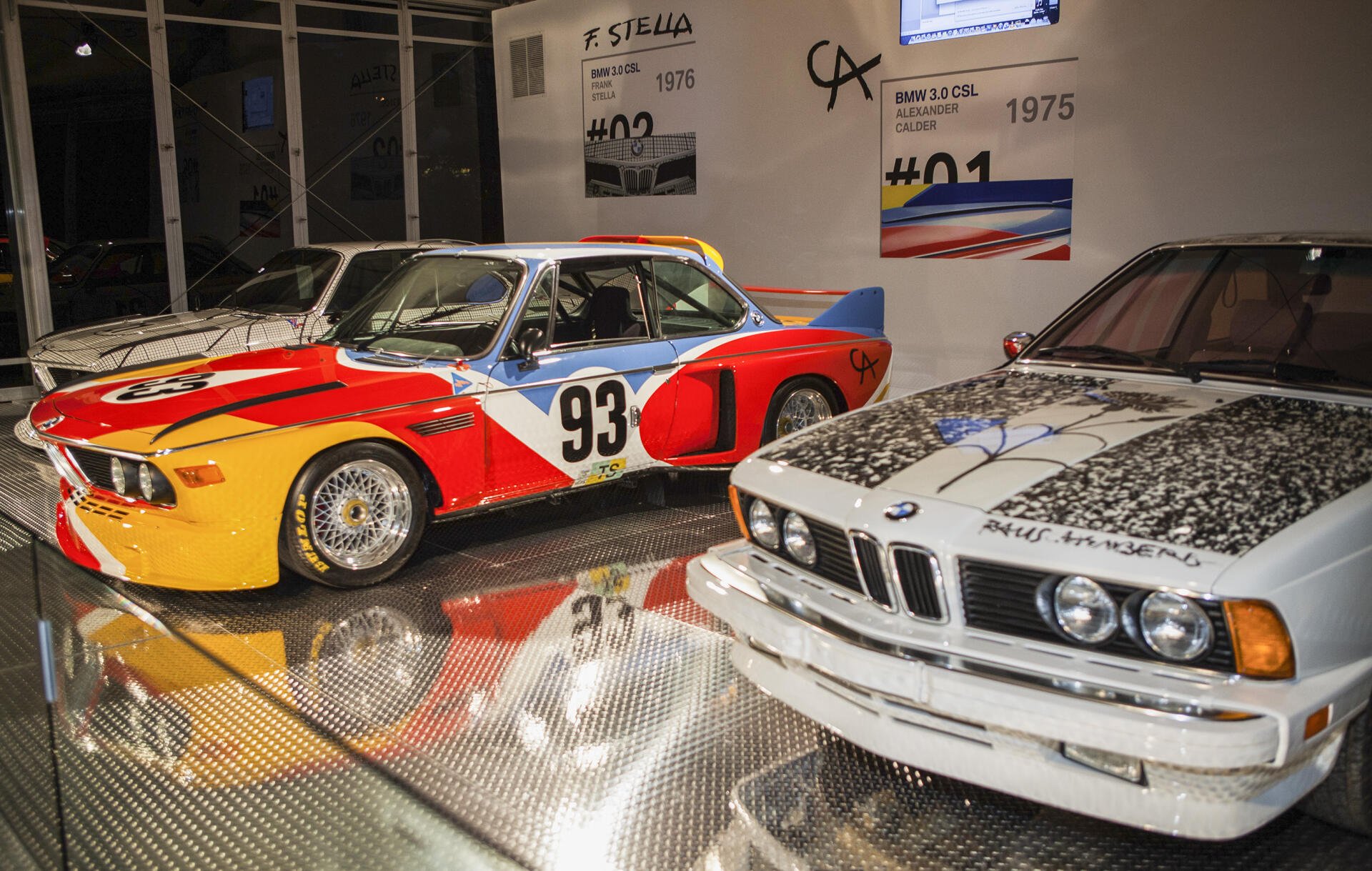 A striking HD wallpaper featuring a BMW 635CSi and a BMW 3.0 CSL, showcasing their iconic designs in a modern exhibit setting, highlighted by vibrant colors and reflections.