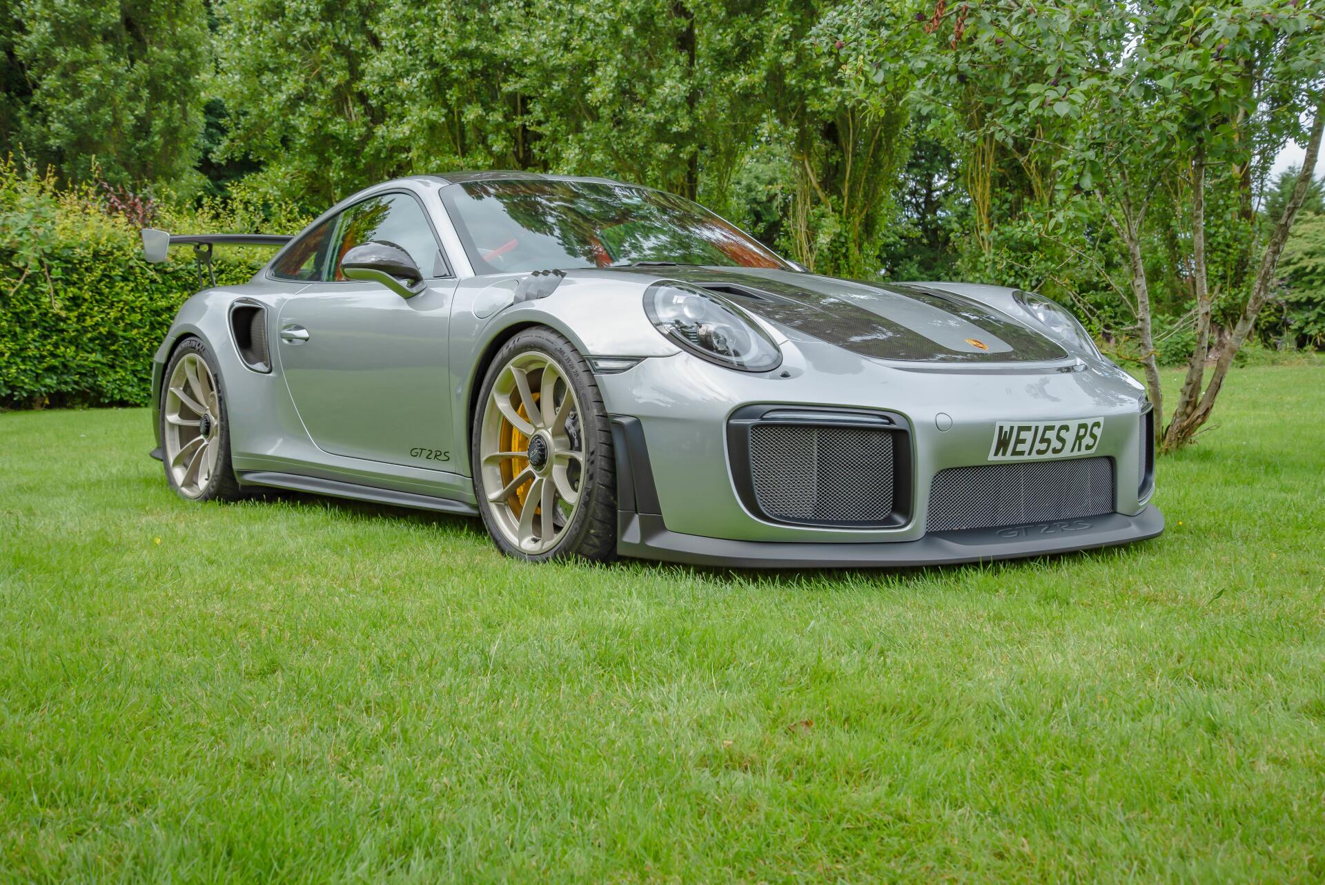Silver Porsche sports car on a green lawn with trees, high-detail 5K Ultra HD PC desktop wallpaper and background highlighting sleek bodywork and gold brake calipers.