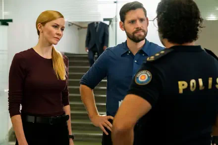 A scene from the TV show *FBI: International*, featuring two agents engaging in a serious conversation with a police officer. The backdrop includes a modern interior setting.