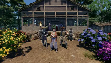 A vibrant scene from the video game Sengoku Dynasty, featuring characters in traditional attire standing in front of a wooden house, surrounded by colorful flowers and lush greenery.