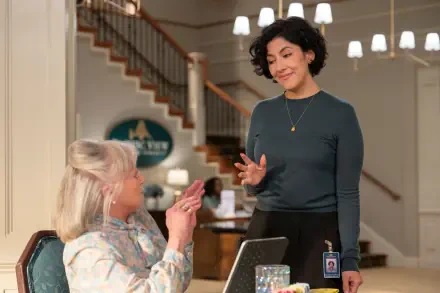 A scene from the TV show A Man on the Inside, featuring two women engaged in conversation. One stands, animated and expressive, while the other listens intently at a table.