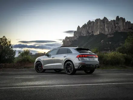 A stunning 4K Ultra HD wallpaper featuring a sleek Audi RS Q8 parked on a scenic road, with dramatic mountains in the background under a colorful sky at dusk.