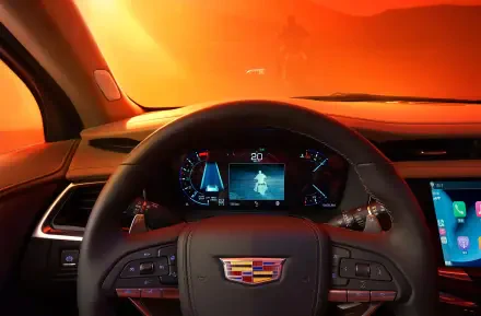 The image showcases the interior of a Cadillac XT6, featuring a vibrant orange backdrop and a view of the dashboard with advanced controls and display screens.