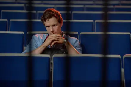 A still from Dexter: Original Sin featuring Patrick Gibson seated alone in an empty theater, hands clasped, with vibrant blue seats in the background. 4K Ultra HD quality.