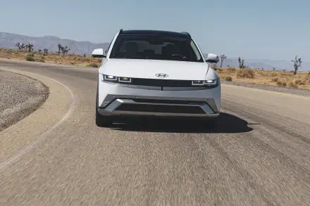 A sleek Hyundai IONIQ 5 drives along a curved road, framed by a desert landscape. This 4K Ultra HD image captures the car's modern design and dynamic stance.