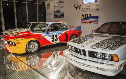A striking HD wallpaper featuring a BMW 635CSi and a BMW 3.0 CSL, showcasing their iconic designs in a modern exhibit setting, highlighted by vibrant colors and reflections.