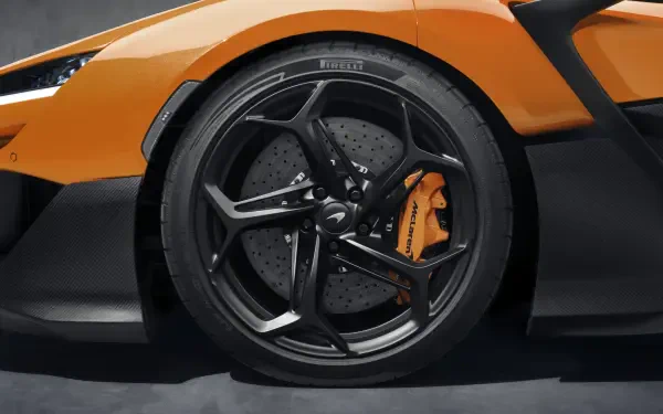 A close-up of a McLaren W1 vehicle, showcasing its sleek orange exterior and distinctive multi-spoke black wheel, set against a dark background in stunning 8K Ultra HD detail.