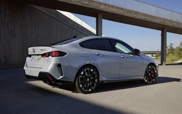 A sleek BMW M235 Gran Coupe parked against a modern architectural backdrop, showcasing its dynamic design and sporty features in an HD desktop wallpaper format.