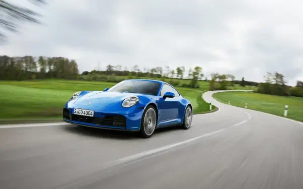 A sleek blue Porsche 911 Carrera speeds along a winding road, surrounded by lush greenery, showcasing its dynamic design and performance. An HD desktop wallpaper for car enthusiasts.